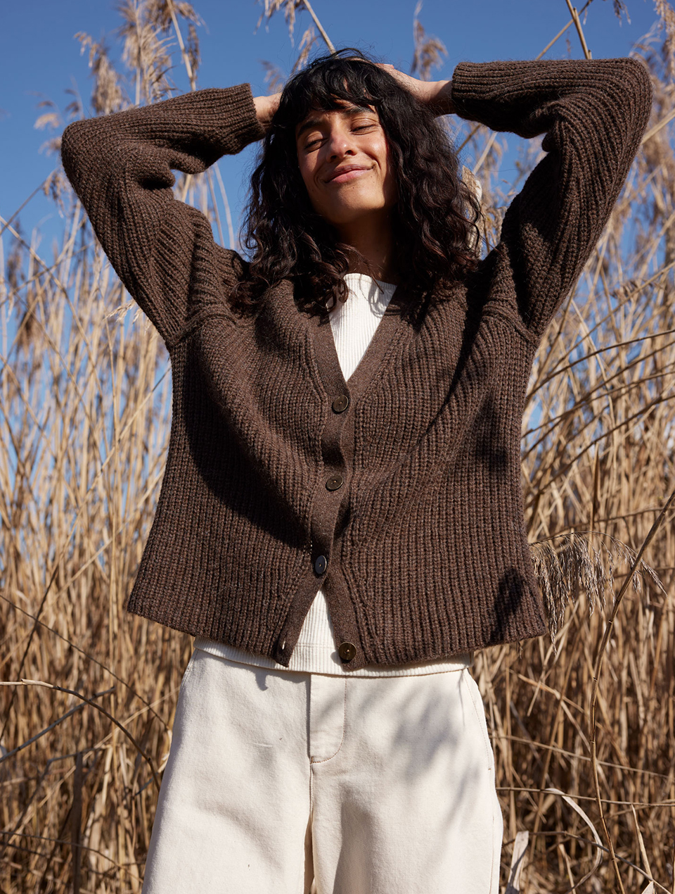 Frau trägt braune Strickjacke und helle Hose in natürlicher Umgebung