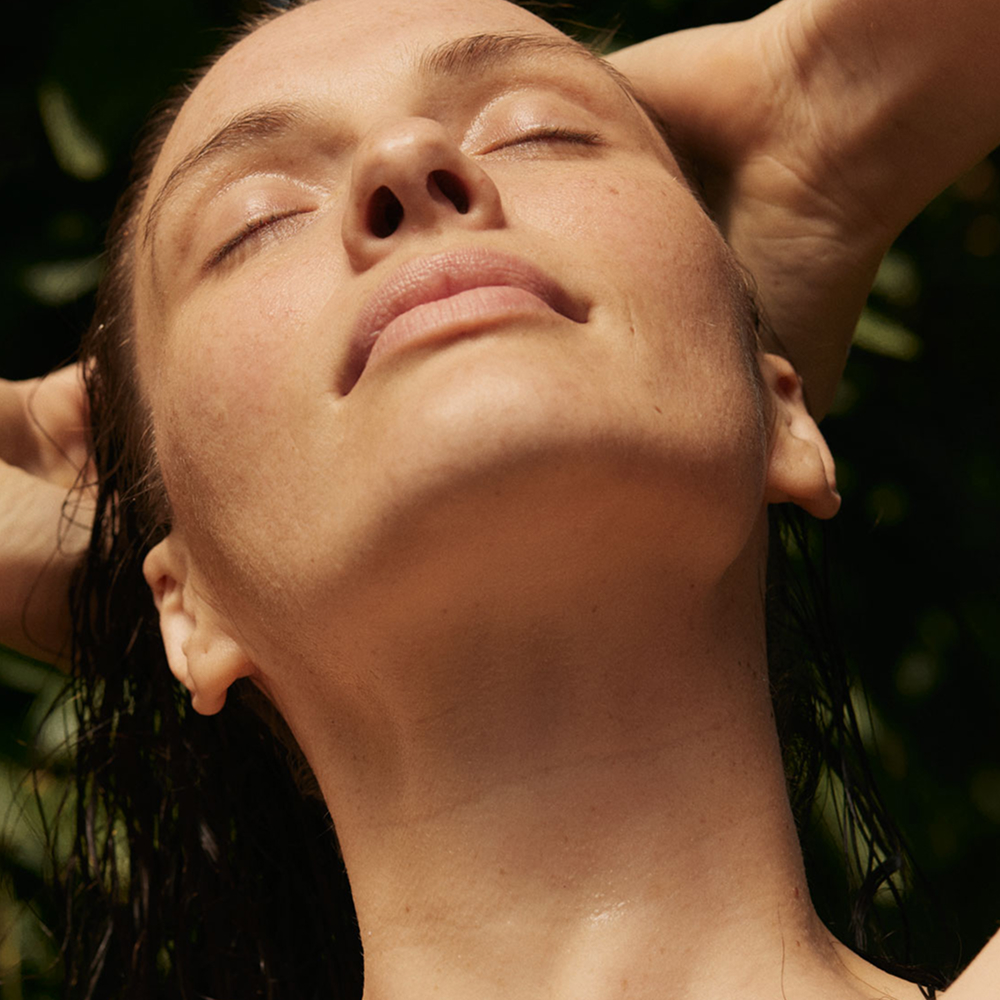 Frau mit geschlossenen Augen und beiden Händen hinter dem Kopf in einer natürlichen Umgebung