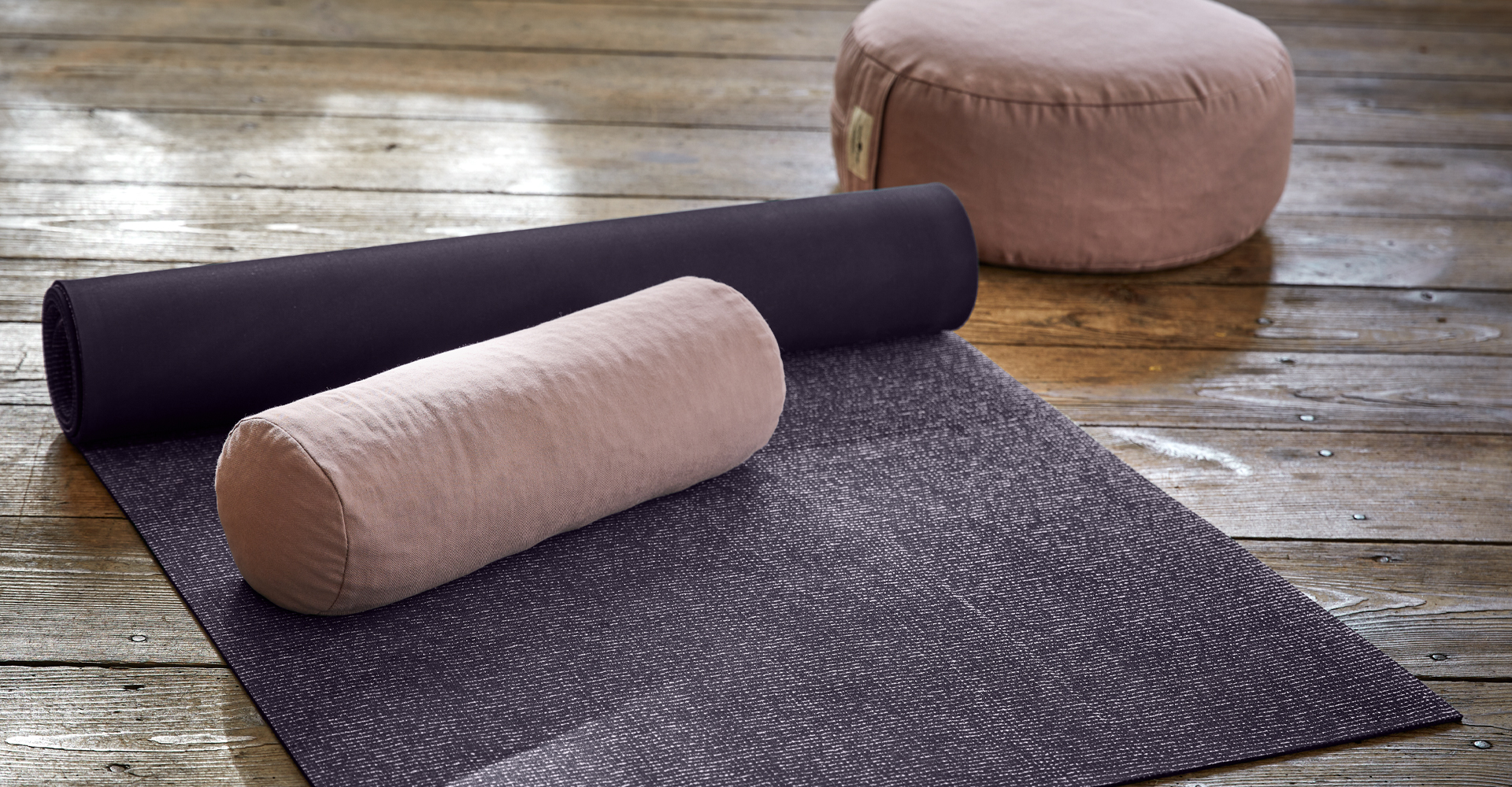 Lila Yogamatte mit rosa Nackenkissen und Yogakissen auf Holzboden in natürlichem Licht