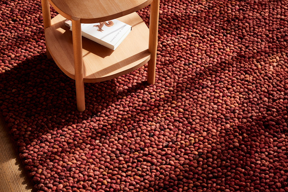 Roter strukturierter Teppich unter kleinem Holztisch im warmen Licht