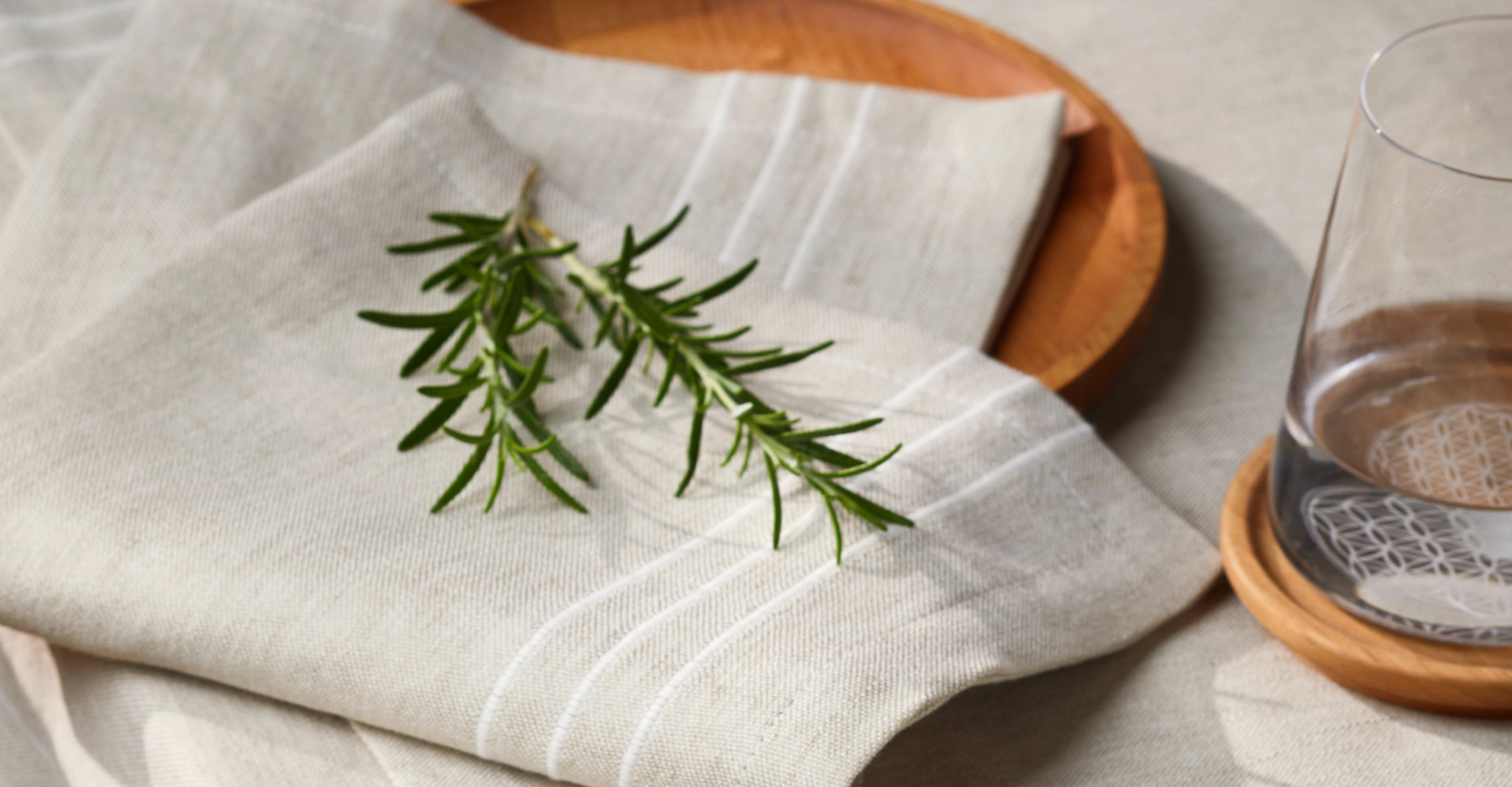 Graue Geschirrtücher auf Holzbrett liegend mit einem Rosmarinzweig