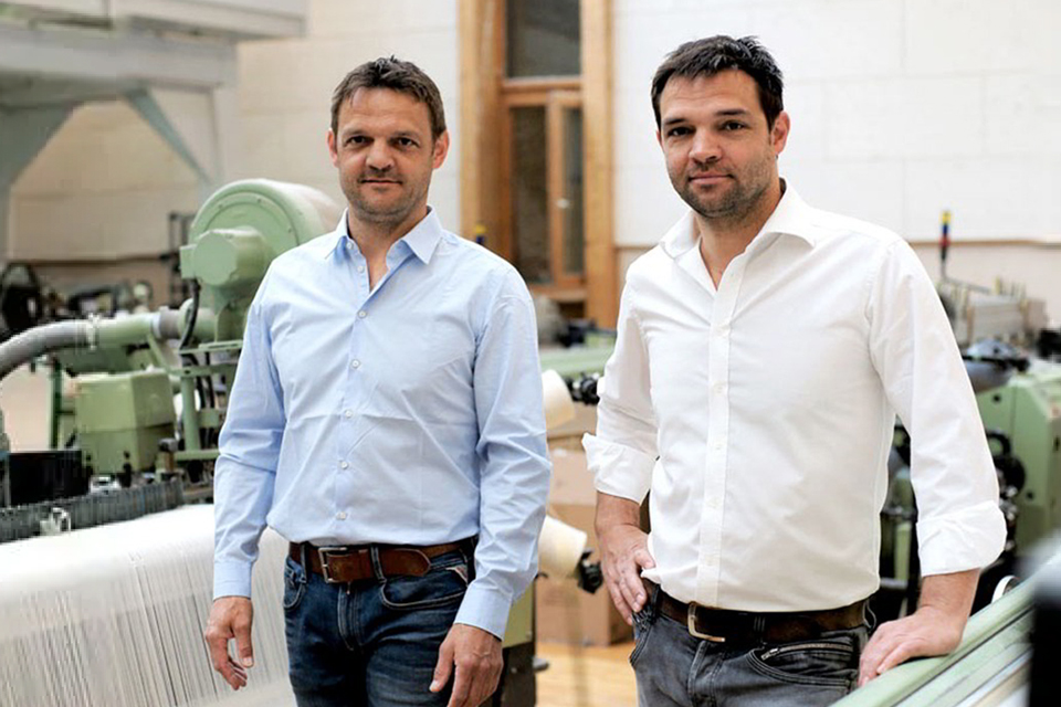 Zwei Männer stehen in Raum mit Webstühlen