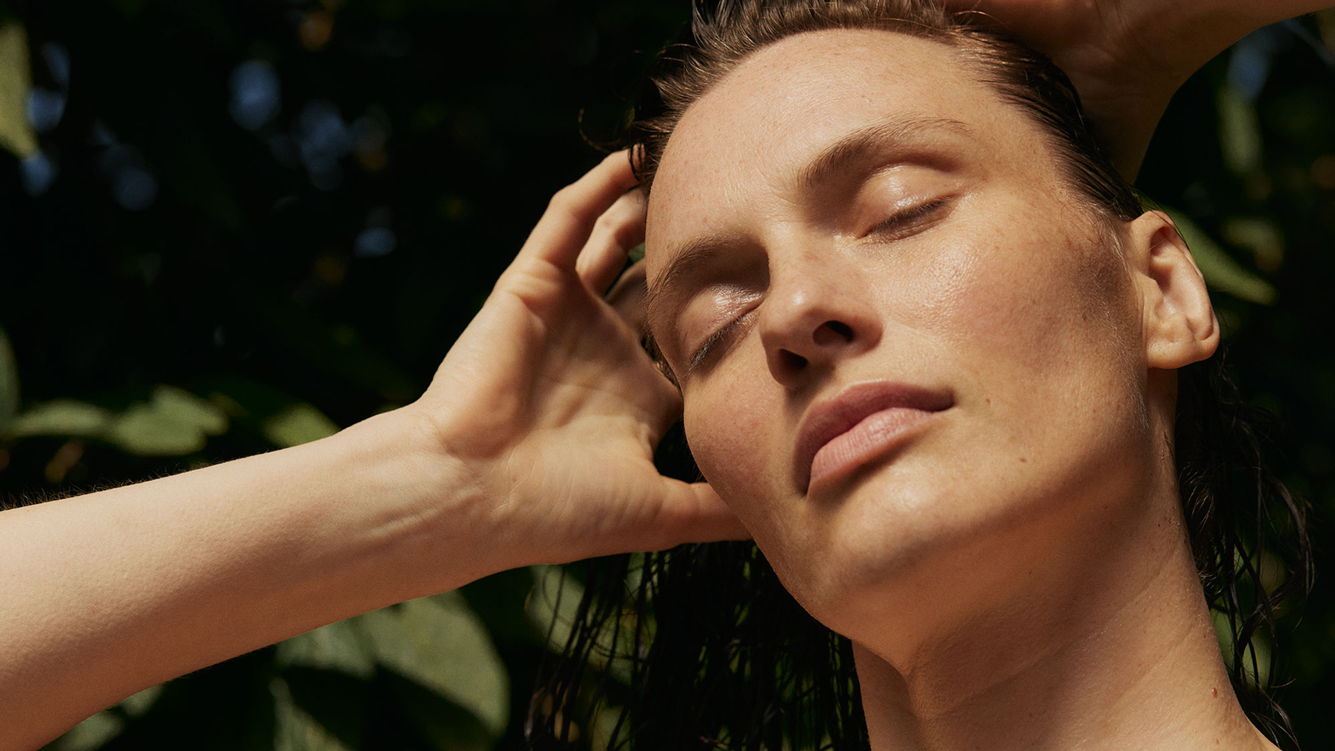 Frau mit geschlossenen Augen und beiden Händen hinter dem Kopf in einer natürlichen Umgebung