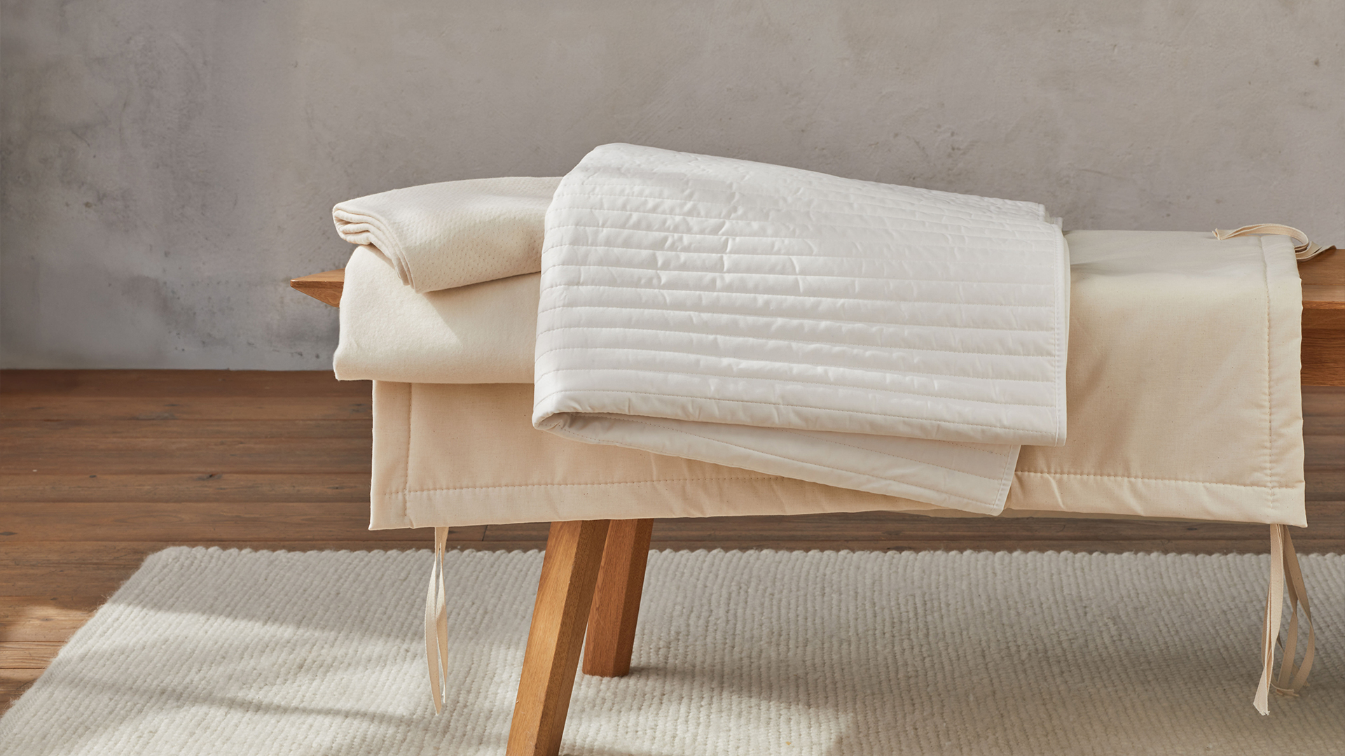 verschiedene Unterbetten liegen auf einer Holzbank