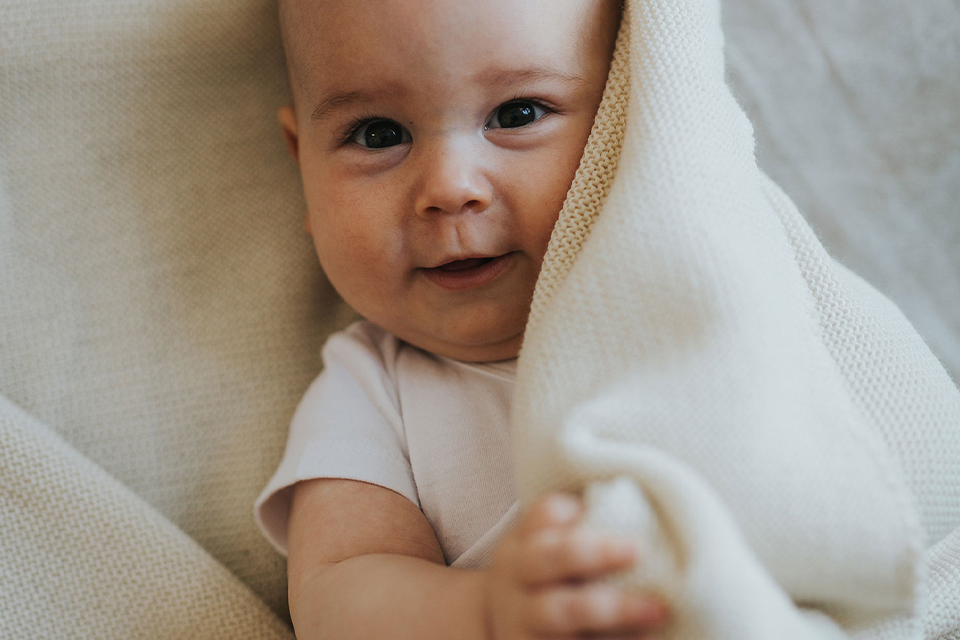 Baby schaut unter weißer Decke hervor