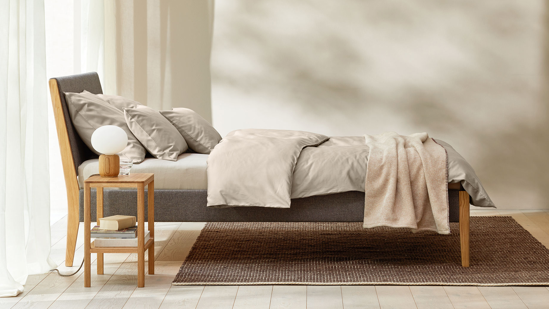 Hochwertiges Bett Almeno mit Bettwäsche vor einem großen bodentiefen Fenster