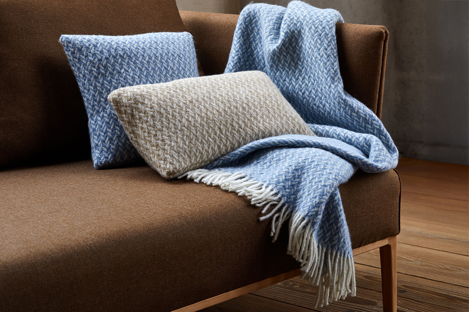 Zierkissen und Wohndecke auf einem braunen Sofa liegend