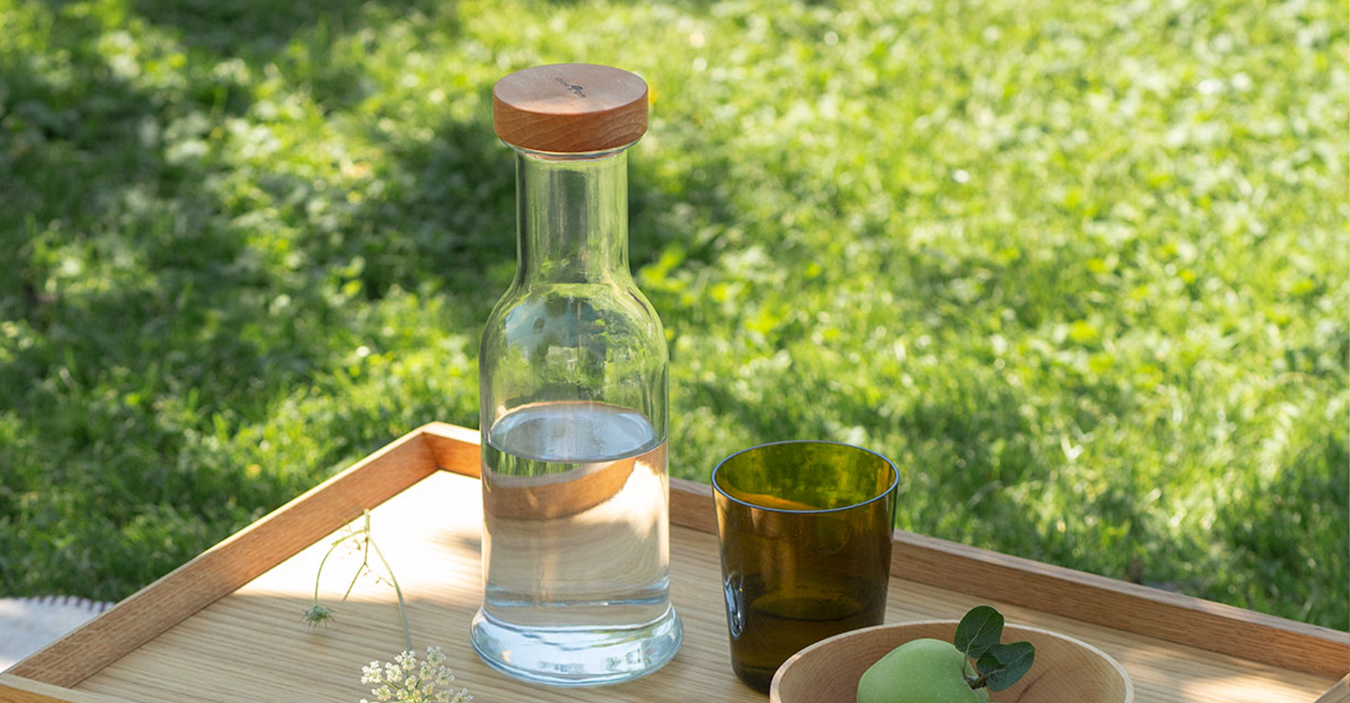 Eine Karaffe und ein dunkles Glas stehend auf einem Holztablett.