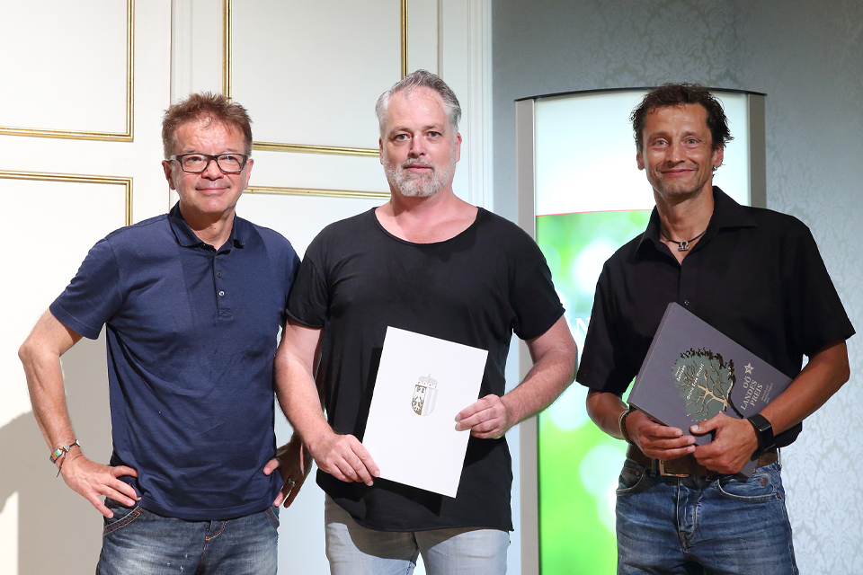 Drei Personen posieren mit einer Urkunde nach Preisverleihung