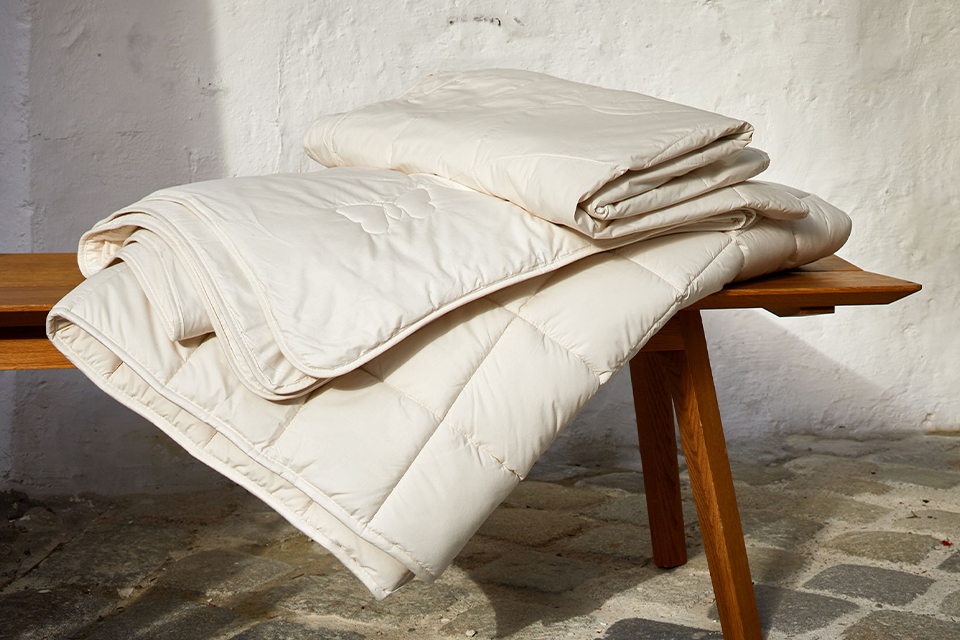 Zwei Bettdecken auf einer dekorativen Holzbank liegend