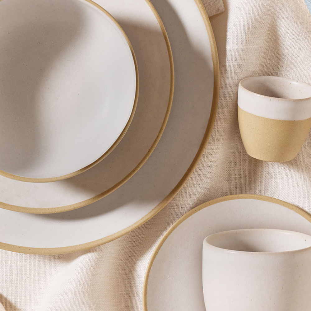 Zwei Teller gestapelt. Darauf steht eine Schüssel. Daneben liegt eine kleine Tasse. Unter der kleinen Tasse liegt eine kleine Schüssel. Darauf eine größere Tasse