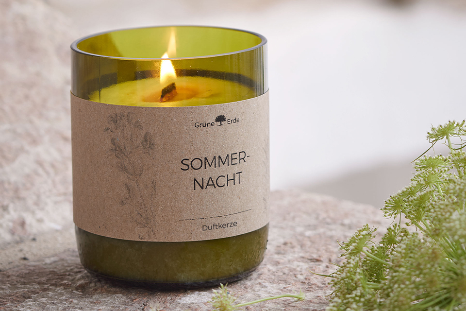 Brennende Duftkerze aus Glas mit natürlicher Dekoration daneben