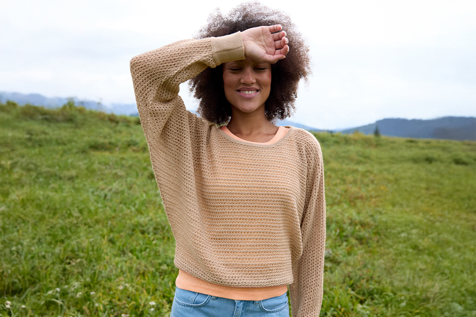 Frau schützt Augen vor Sonne auf Feld, lächelt entspannt