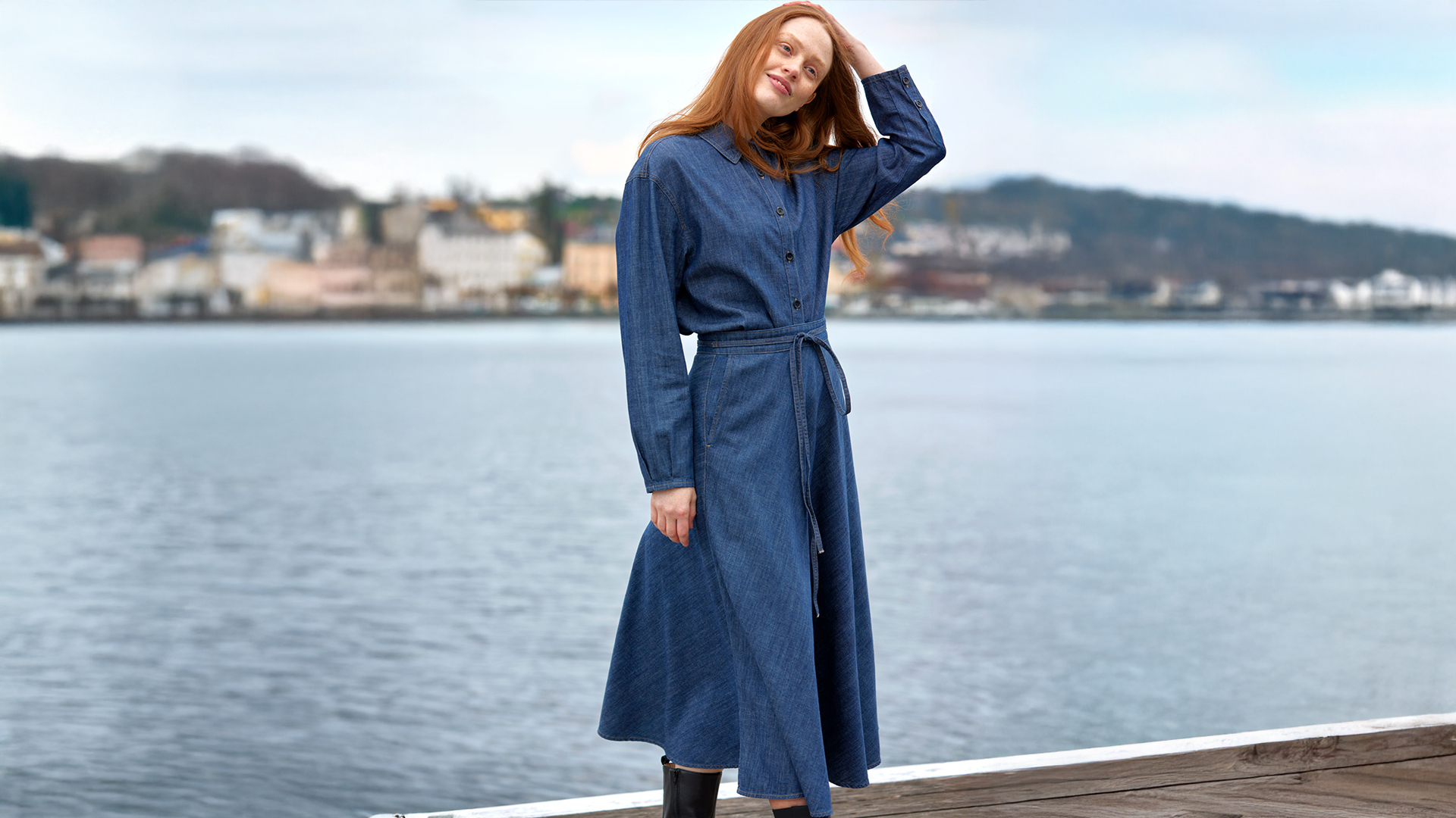 Frau in blauem Mantel steht am Wasserufer