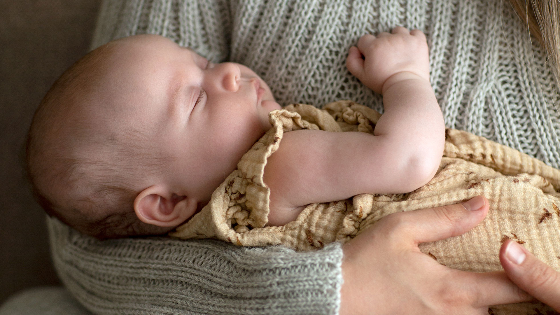 Schlafendes Baby im Arm der Mutter lieigend