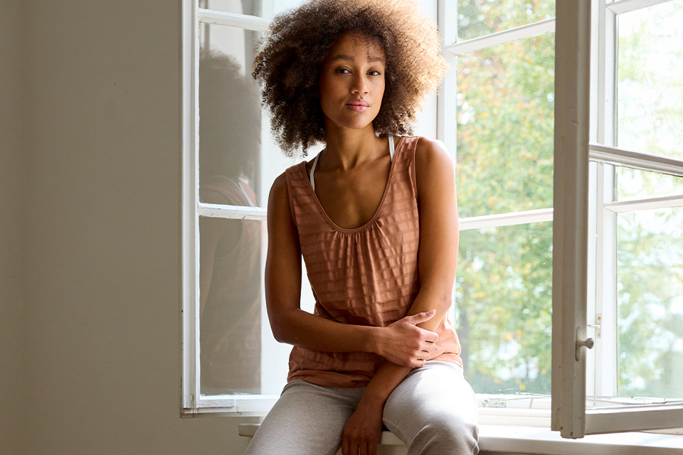Frau sitzt entspannt auf Fensterbank im natürlichen Tageslicht