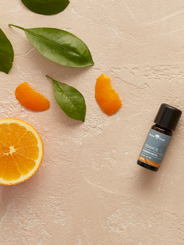 ätherisches Öl und Zucker neben einer Orange und dekorativen Blättern