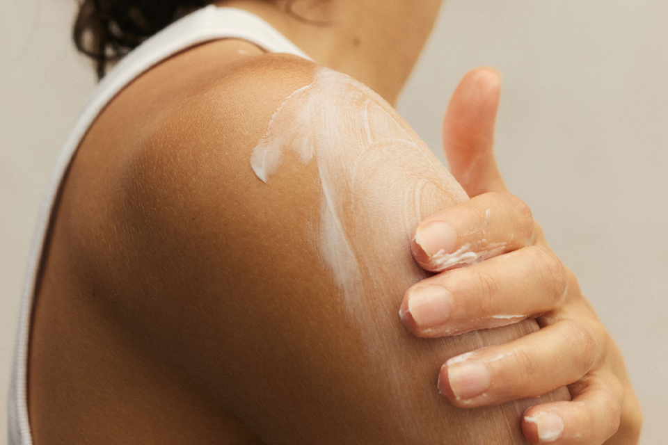eine Frau verteilt Creme auf ihrer Schulter
