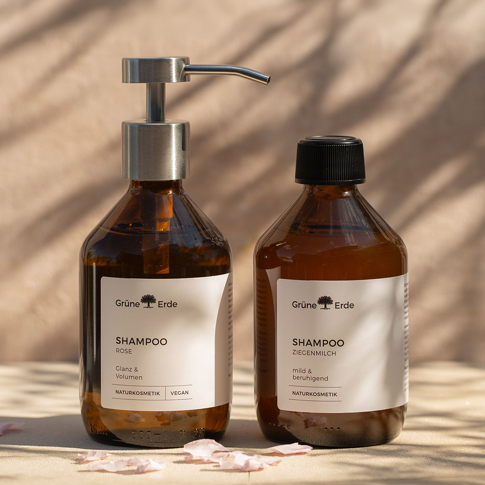 Zwei Shampoo Glasflaschen mit Pumpspender nebeneinander stehend mit dekorativen Blütenblättern