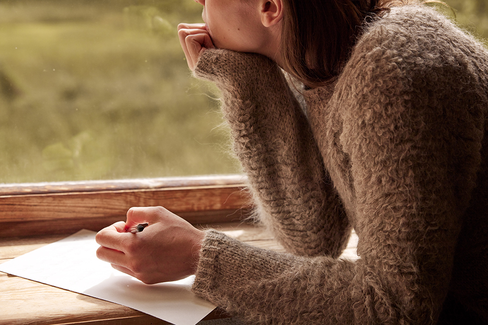 Person schreibt nachdenklich am Fenster mit Blick ins Freie