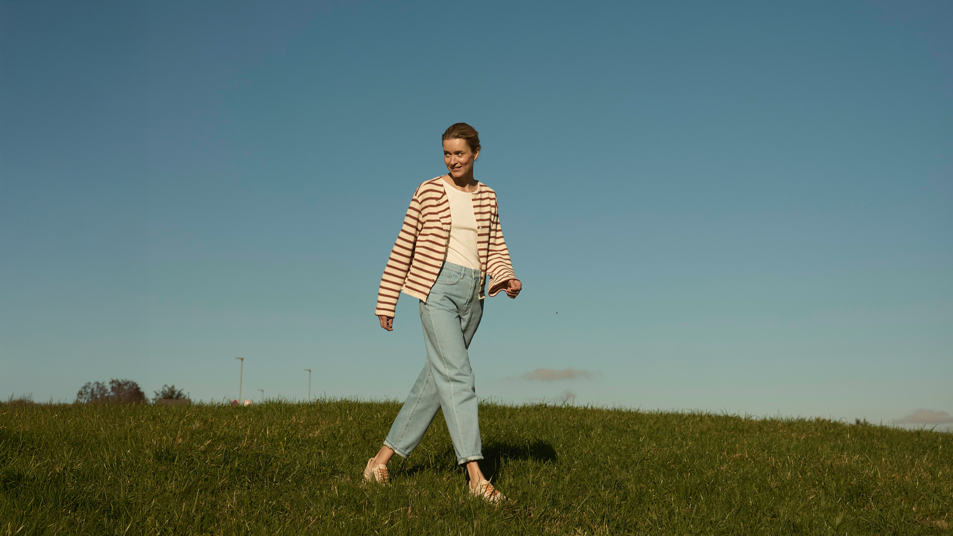 Person spaziert allein über weite Wiese unter blauem Himmel