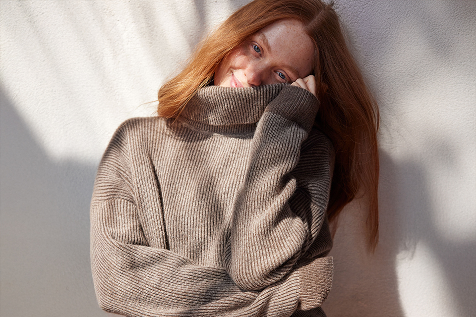 Frau in braunem Pullover neigt ihren Kopf zur Seite