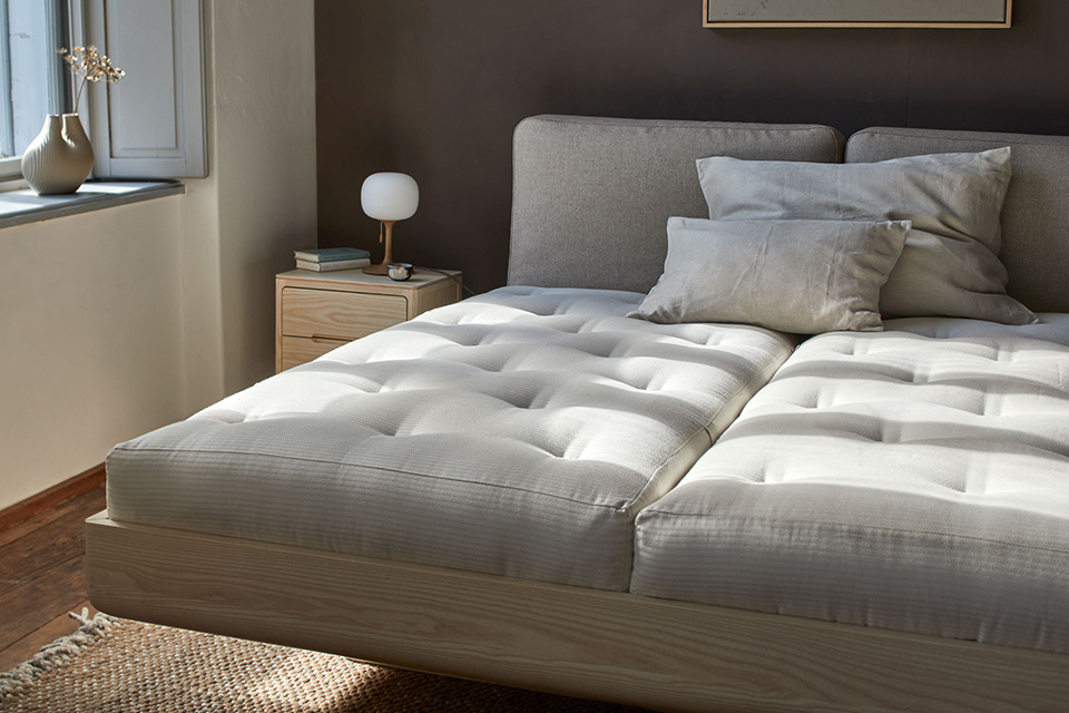 Bett Almara mit Naturmatratzen und Kopfkissen vor dunkler Wand