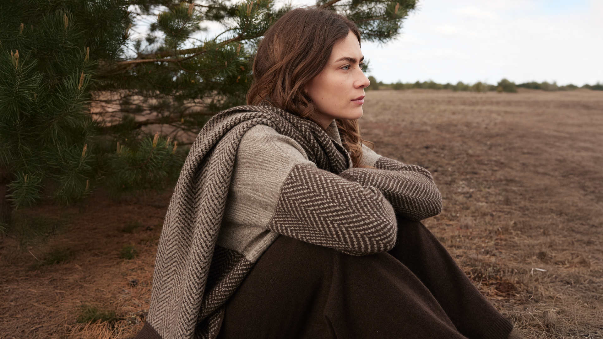 Frau sitzt nachdenklich auf einem Feld in herbstlicher Landschaft