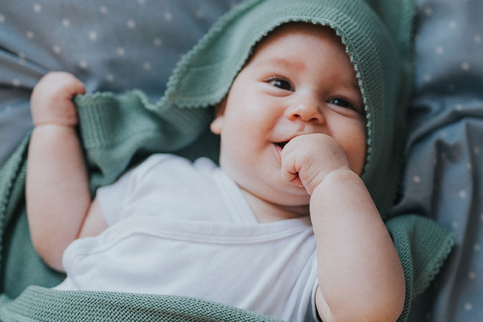 Baby mit grüner Decke lächelt und nuckelt an der Hand