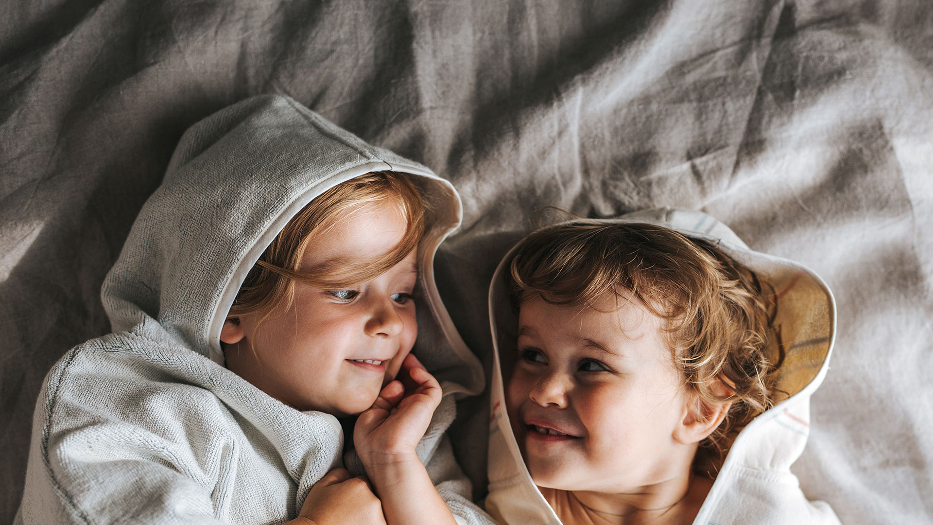 Zwei Babys liegen nebeneinander und schauen sich lächelnd an