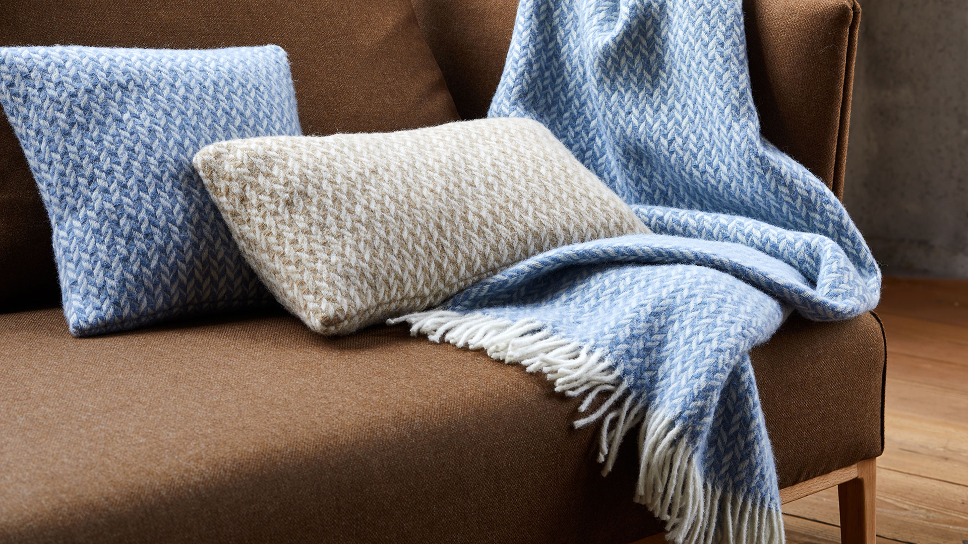 blaue und graue Zierkissen und eine blaue Wohndecke liegen auf einem braunen Sofa