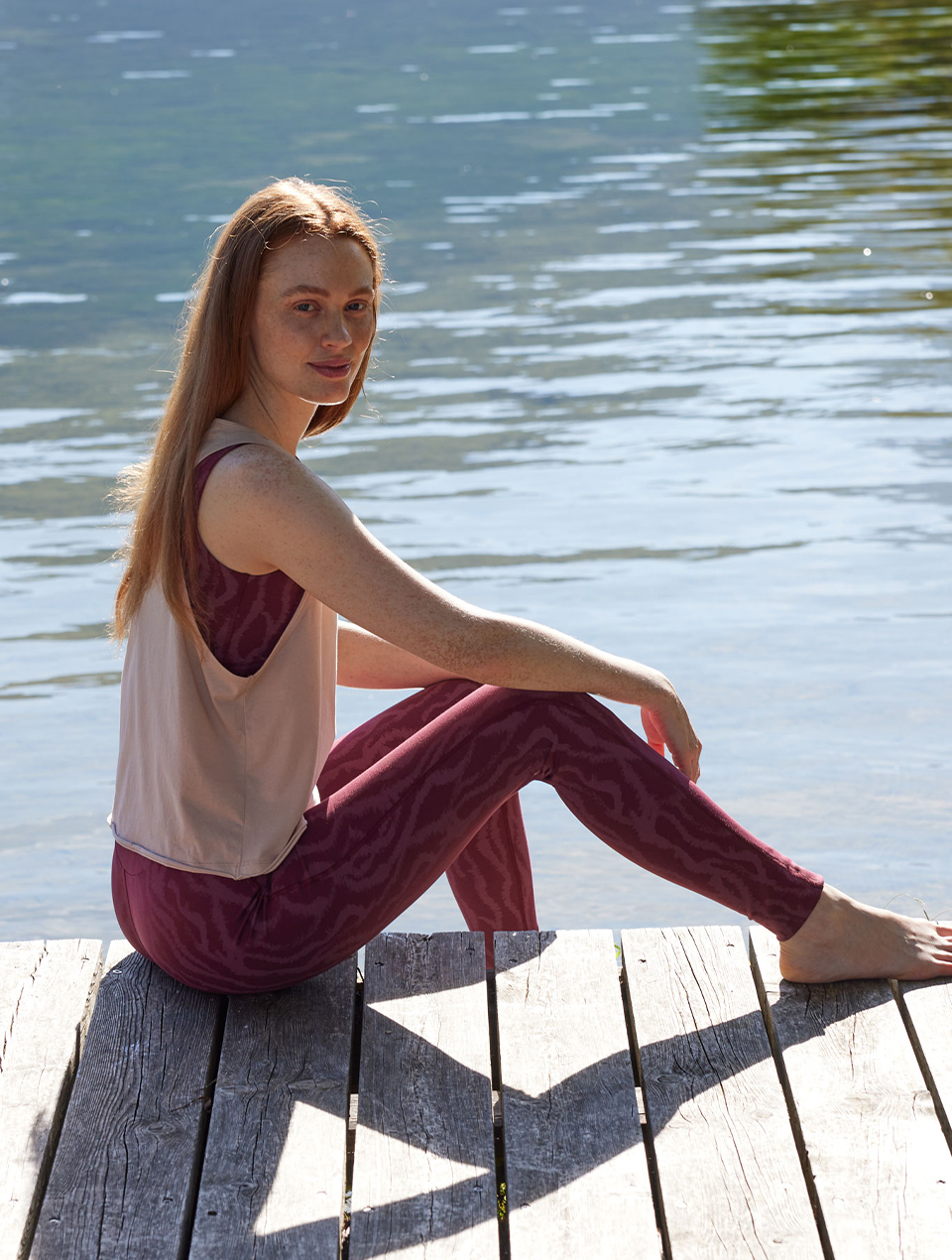 Frau sitzt am Seesteg in roter Leggings und beigem Top