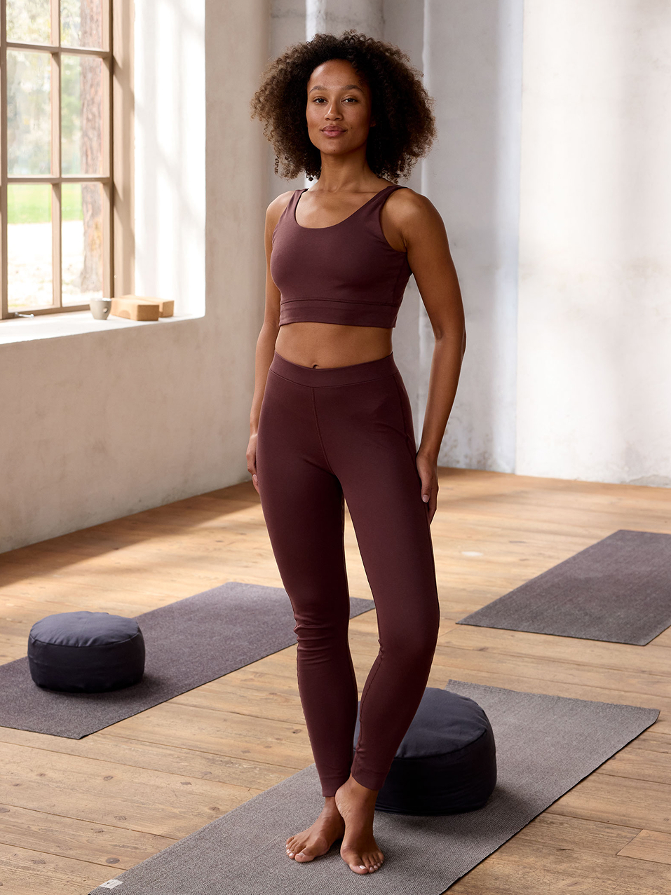 Frau steht auf einer Yogamatte und trägt eine Leggings und einen Yogabra