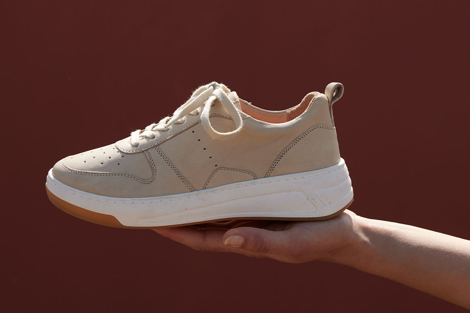 Beiger Sneaker wird stilvoll vor warmem Hintergrund präsentiert