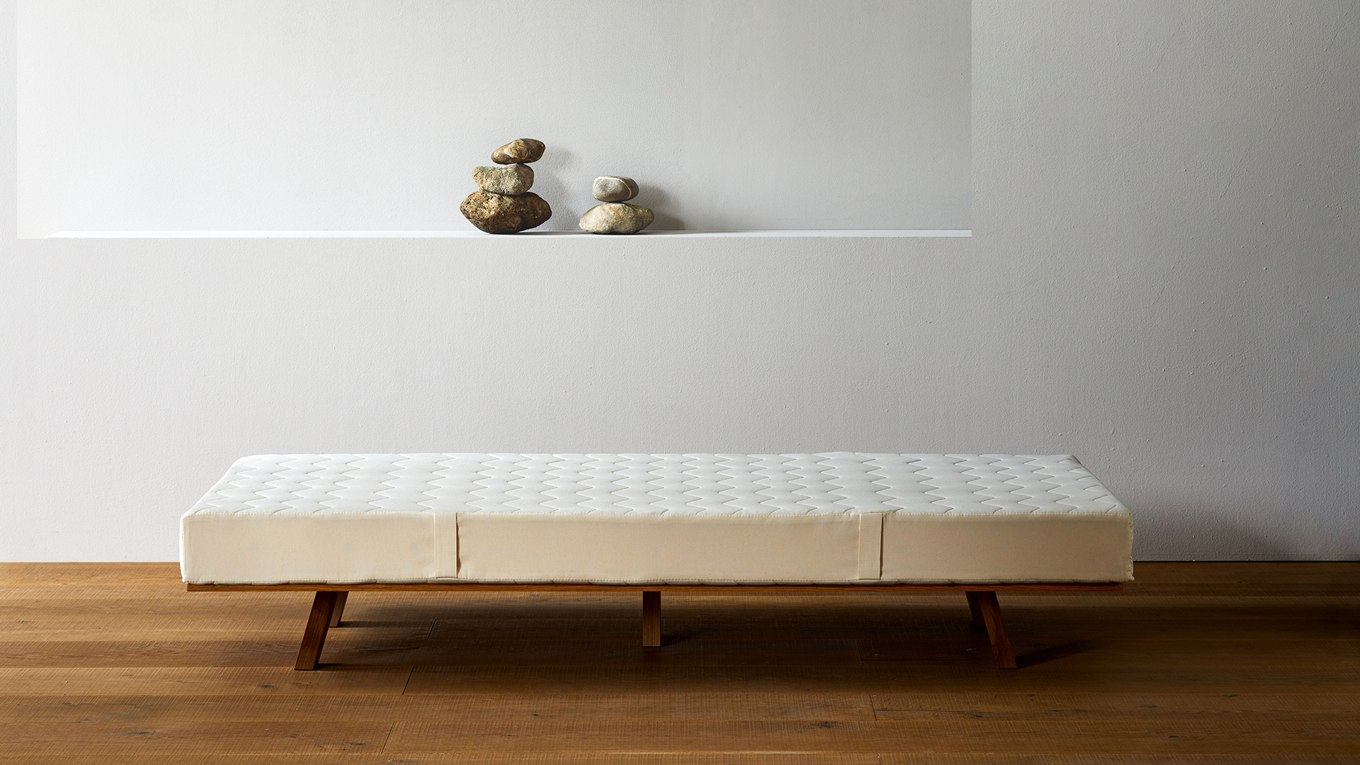 Naturmatratze auf dunklem Holzgestell vor weißer Wand