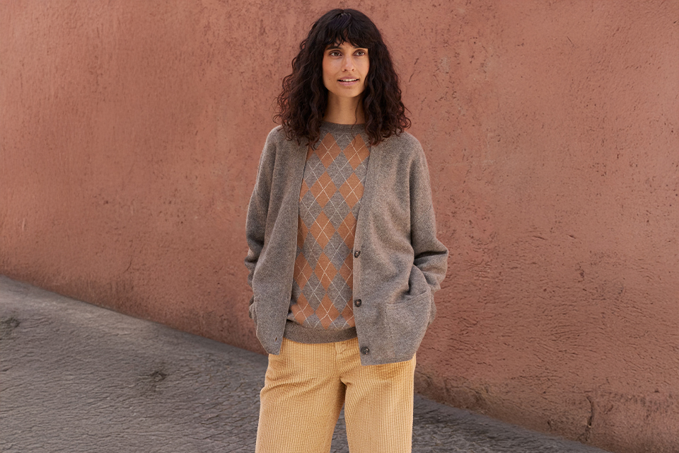 Frau in grauer Weste  steht vor einer Wand