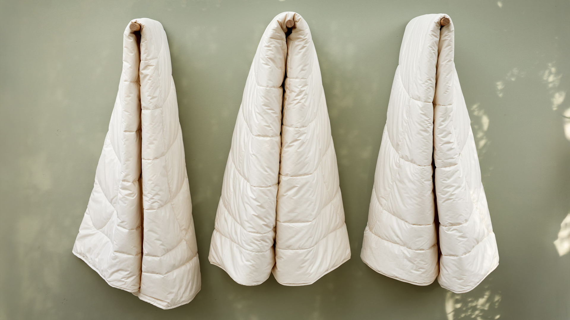 Drei ökologische Schlafdecken hängen an Holzstäben vor einer grünen Wand