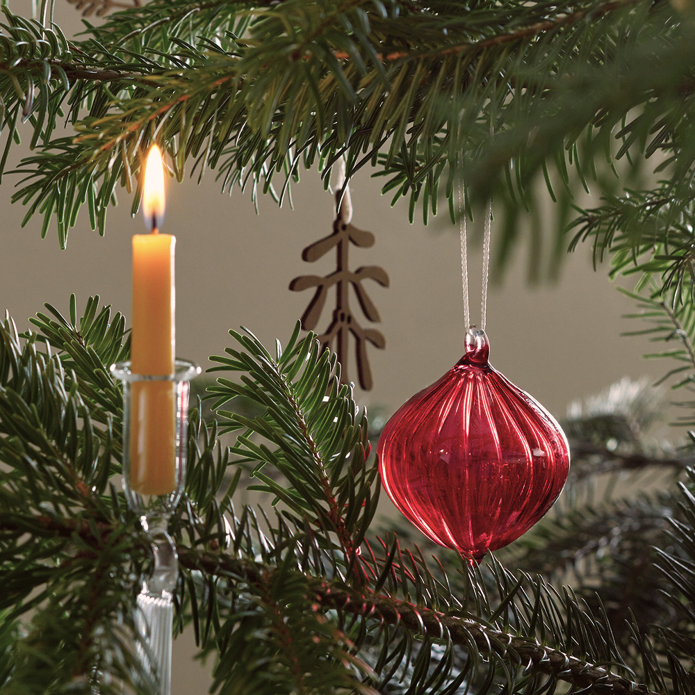 Gebe Kerze und rote Christbaumkugel hängen am Baum