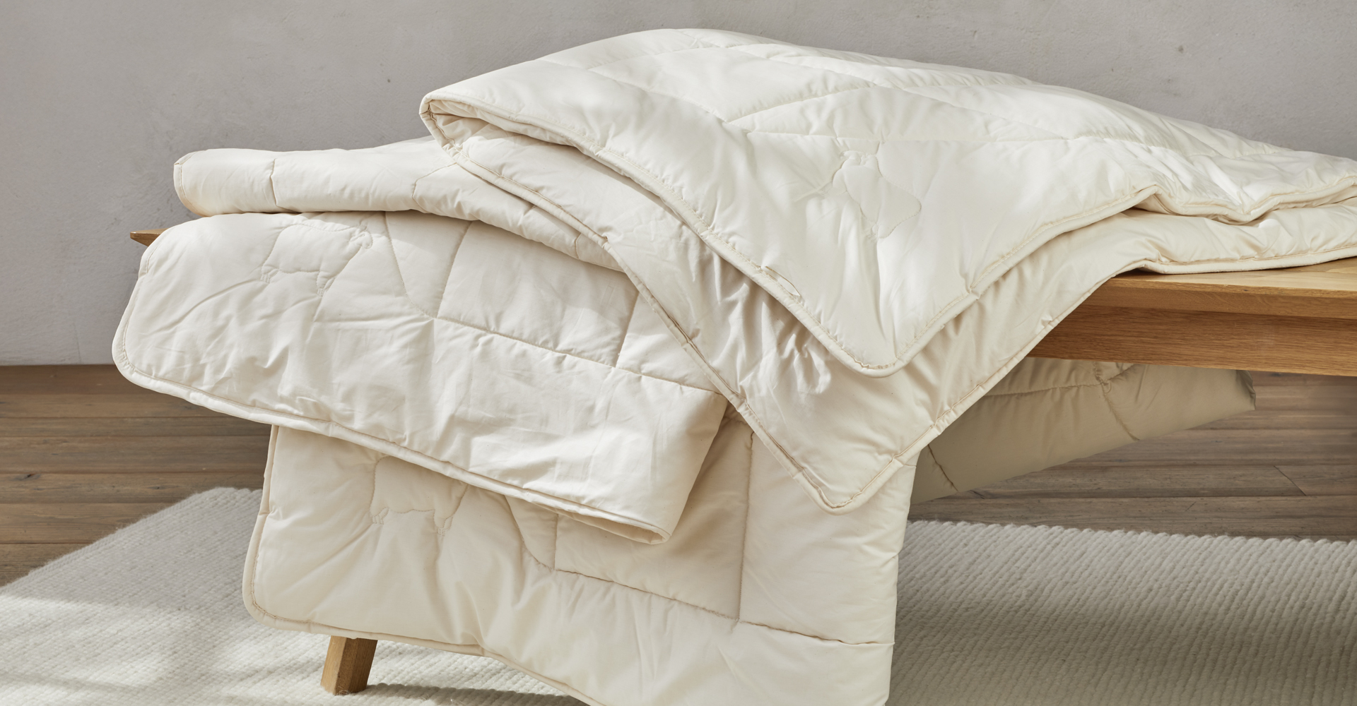 verschiedene Bettdecken liegen auf einer Holzbank