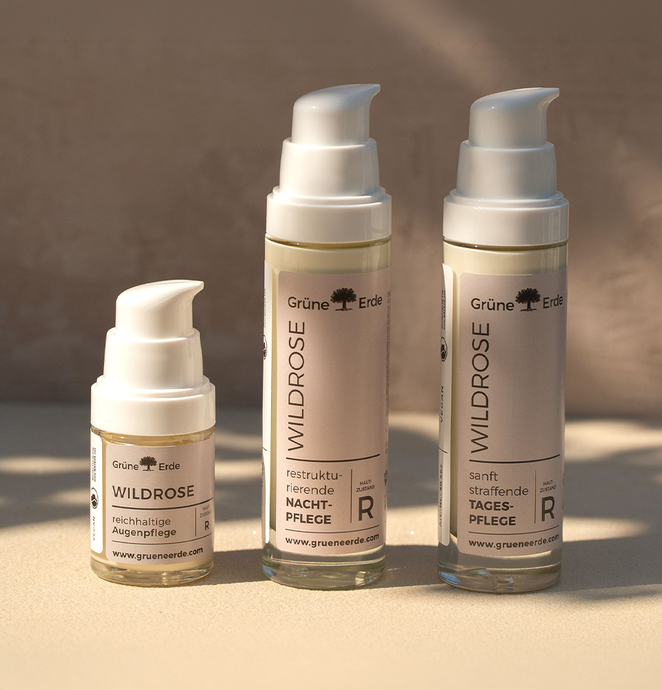 Drei Wildrose Hautpflegeflaschen mit Pumpspendern auf heller Oberfläche.