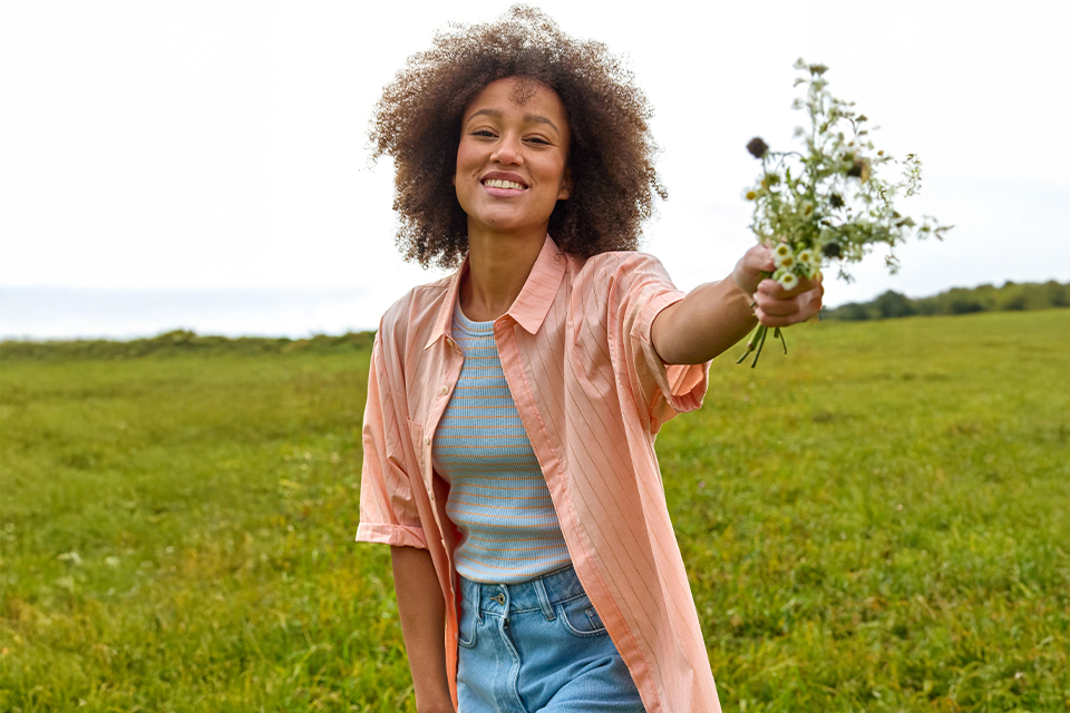 Frau trägt rosa Hemd und Jeans und hält Blumen in der Hand