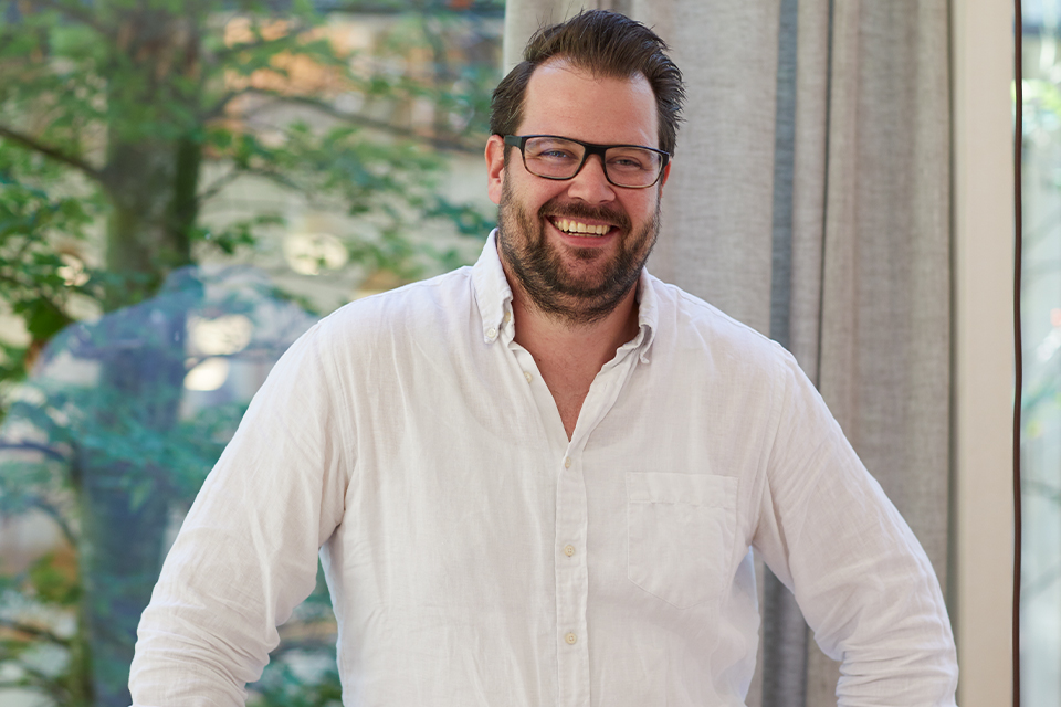 Freundlicher Mann mit Brille steht entspannt vor Fenster im Innenraum