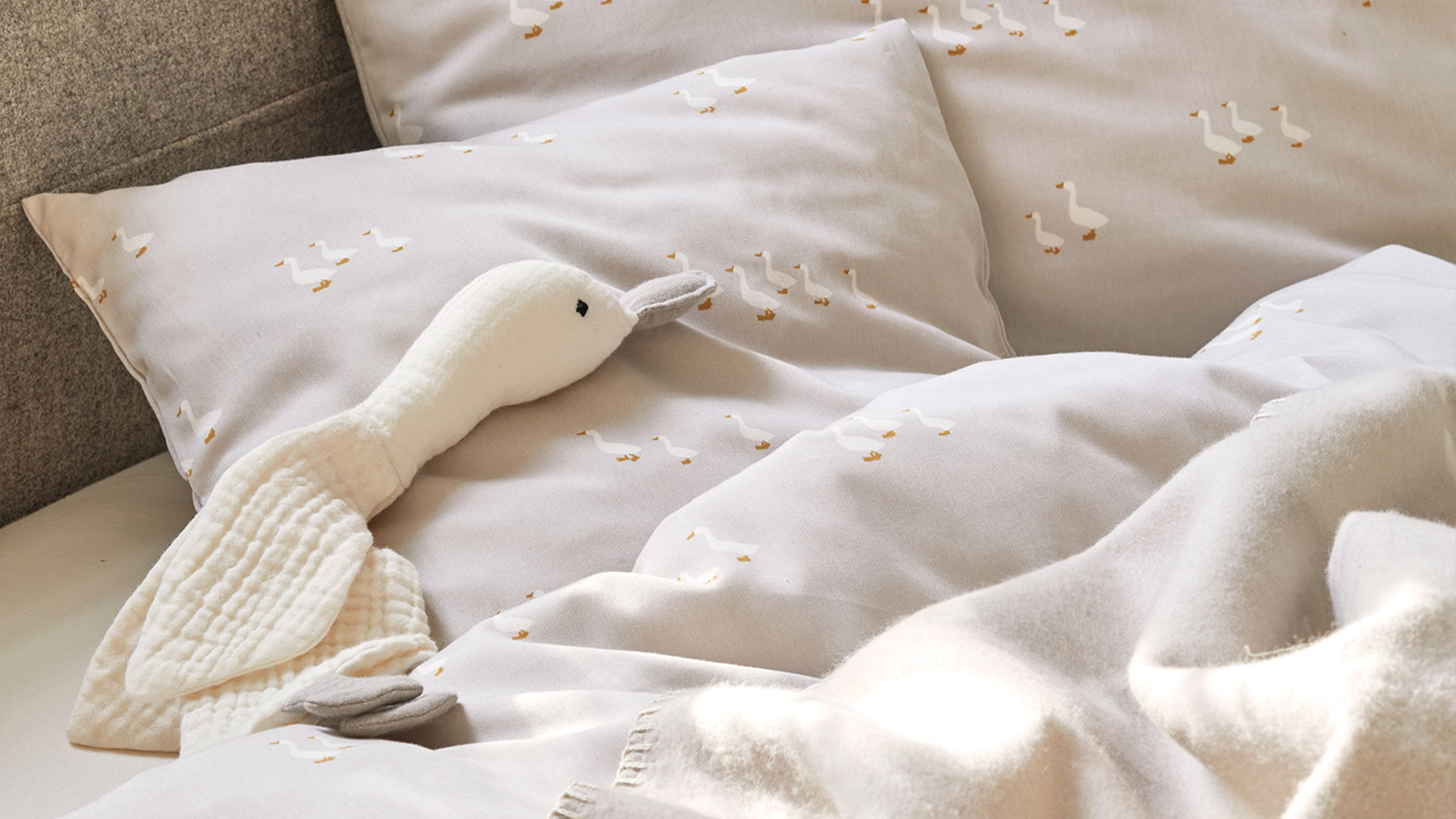Graue Bettwäsche mit Gänsedesign und Kuschelgans auf dem Bett liegend