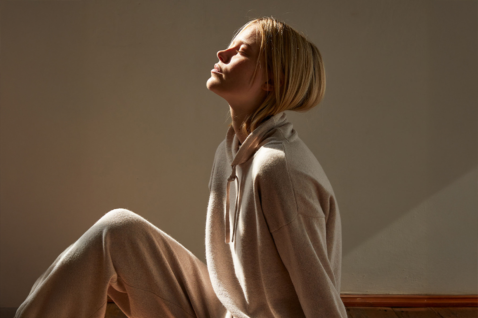 Frau sitzt entspannt mit geschlossenen Augen vor einer Wand