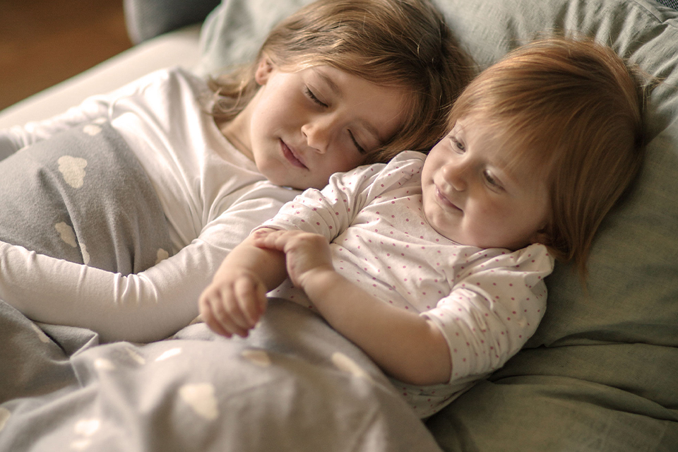 Zwei Kinder liegen im Bett ein Kind schläft das andere schaut ruhig daneben