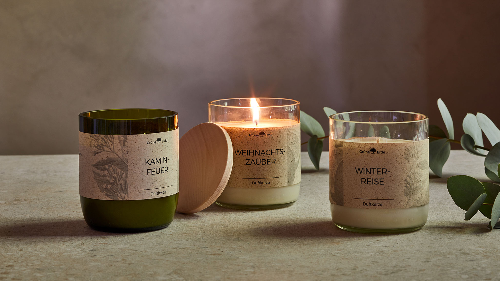 Drei Duftkerzen auf einem Tisch stehend mit einem dekorativen Baumzweig