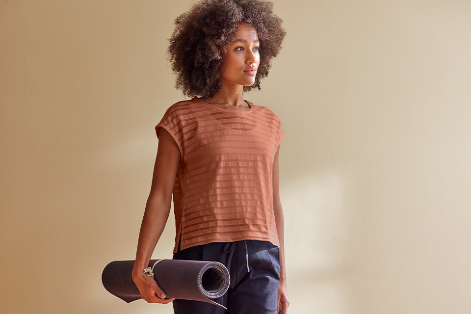 Frau hält Yogamatte und trägt bequemes, elastisches Outfit