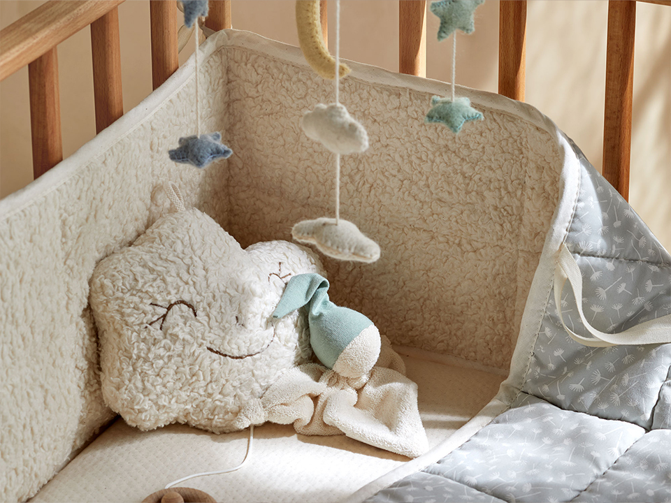 Gitterbettumrandung in blau grau, Filzmobile mit Wolken und Sternen, eine Spieluhr in Wolkenform und ein Schmusewichtel mit grüner Mütze