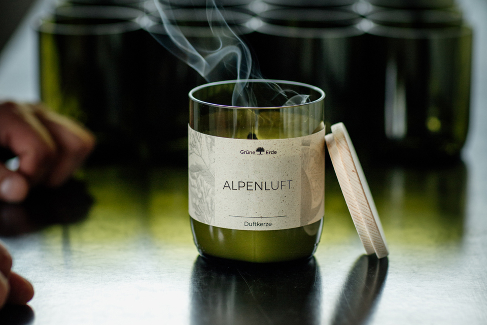 Grüne Kerze mit verglühendem Docht vor leeren Kerzengläsern stehend