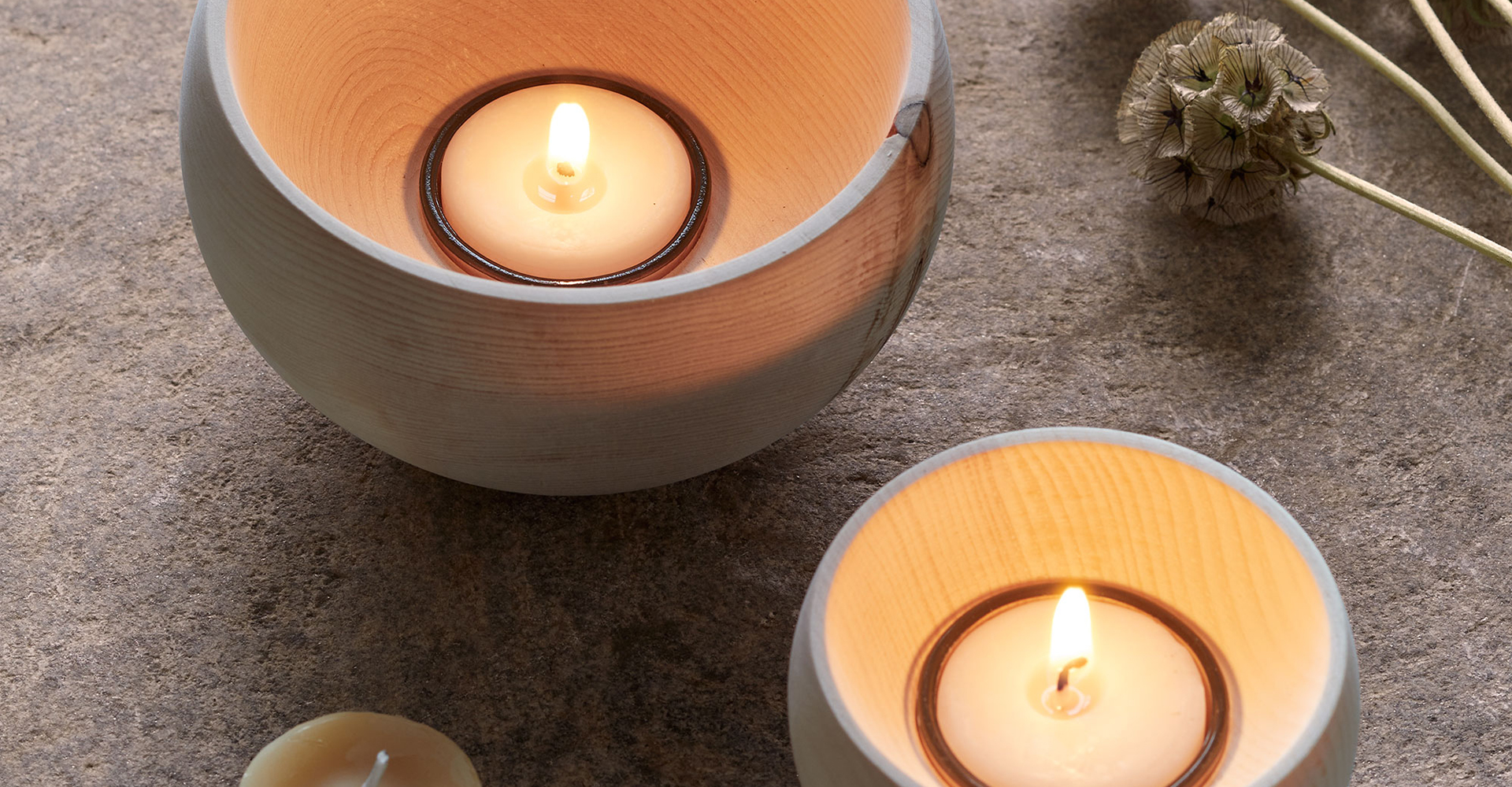 Brennende Kerzen in Holzschalen mit dekorativem Blümchen auf natürlichem Untergrund